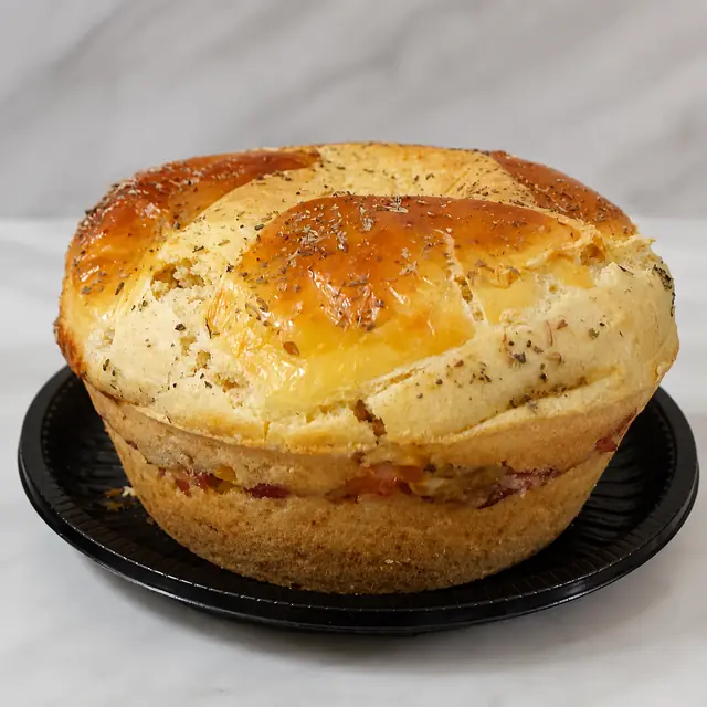 Torta salgada assada com a camada de recheio aparecendo na lateral, coberta por uma massa dourada com orégano.